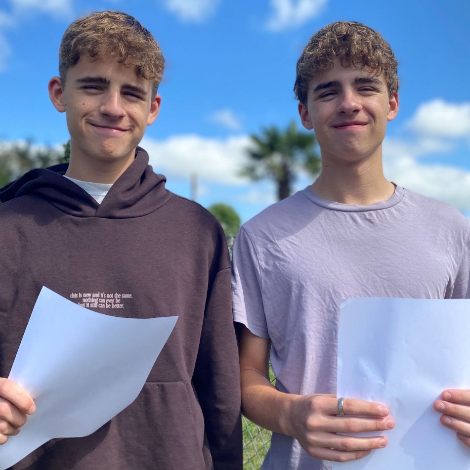 Twins Joe and Tev holding results certificates and smiling
